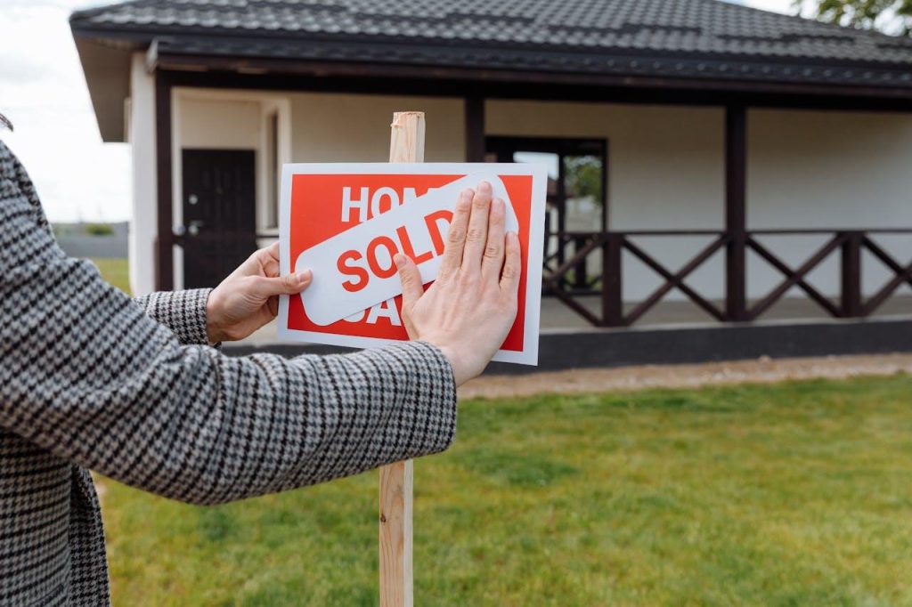 Person placing a "Sold" sign over a "For Sale" sign