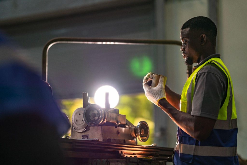 Factory worker using a lamp to inspect a machine part during a power outage in an industrial plant, showing labor challenges and equipment downtime.