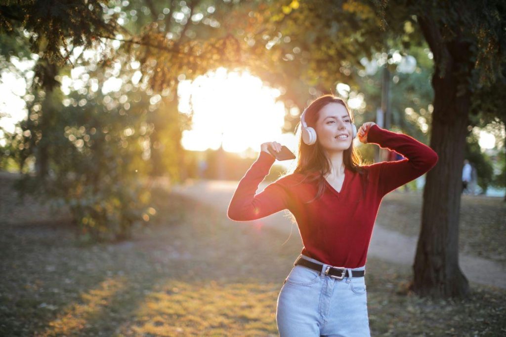 A young woman in a red sweater enjoys music on headphones while walking outdoors, embodying the soundtrack of starting over.