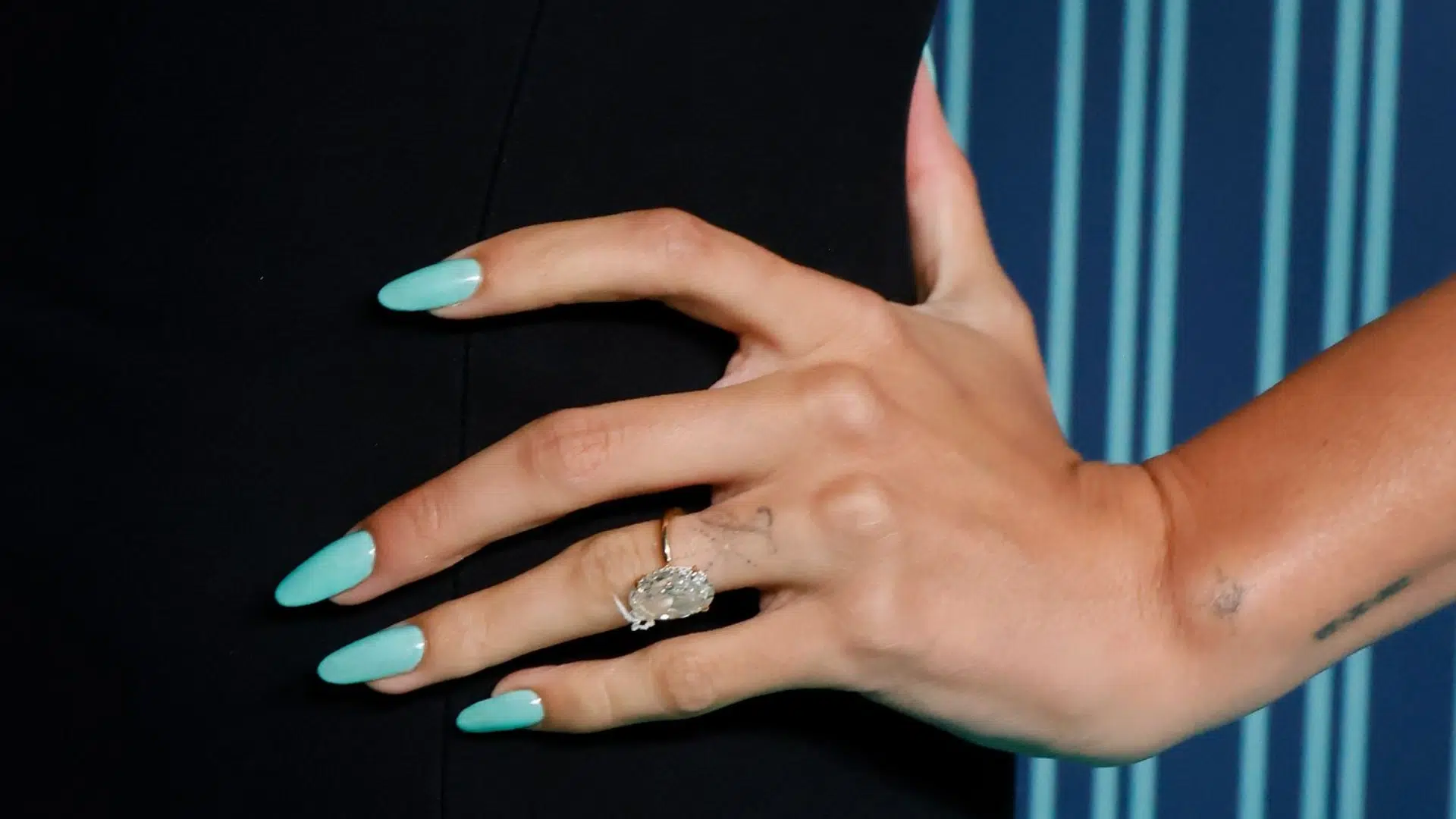 Close-up of Hailey Bieber's oval diamond engagement ring on a thin gold band set