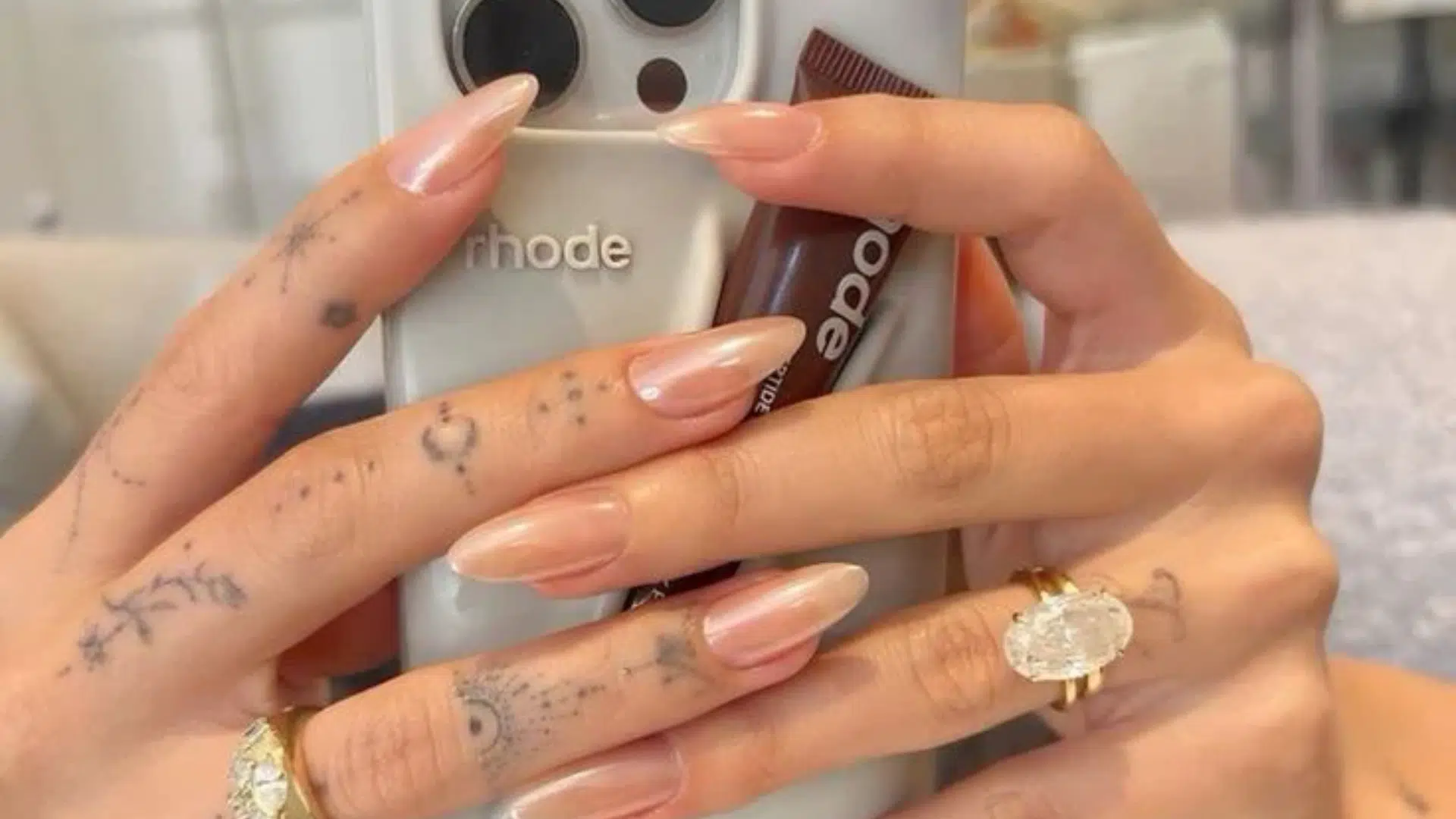 Hailey Bieber holding her phone with oval diamond engagement ring on her hand shown.