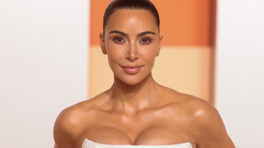 Kim Kardashian posing in a white strapless dress at a formal event backdrop set