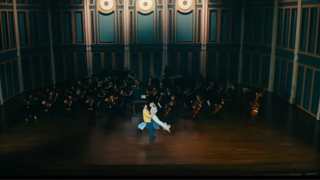 Laura Hand and Larson Rainer dancing on stage in front of full orchestra during cinematic performance on “I Hear a Symphony”