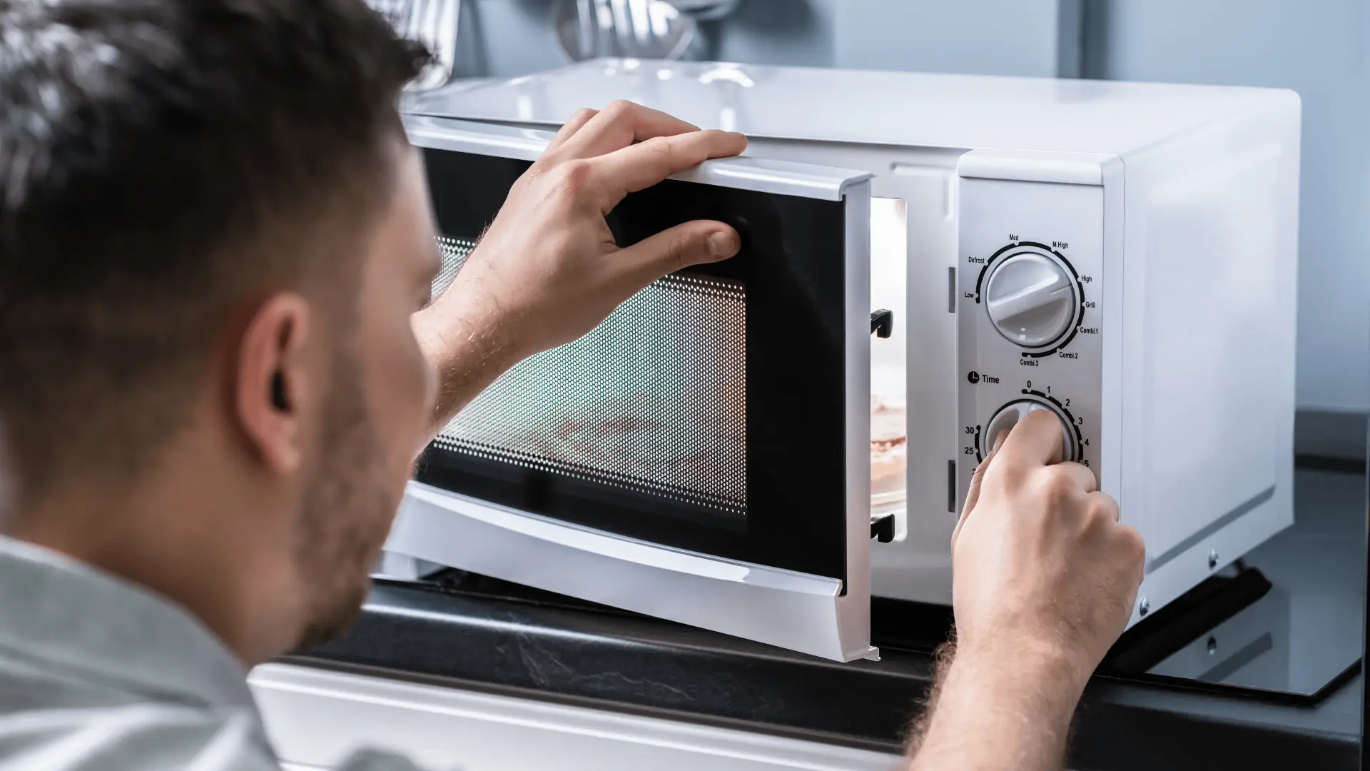Man adjusting settings on a white microwave in a kitchen setting