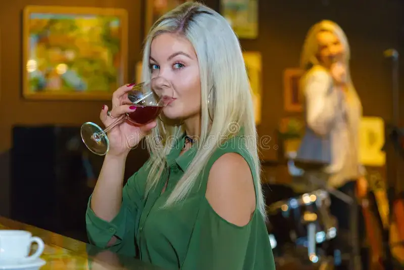 Blonde woman sipping wine at a bar with live music in background