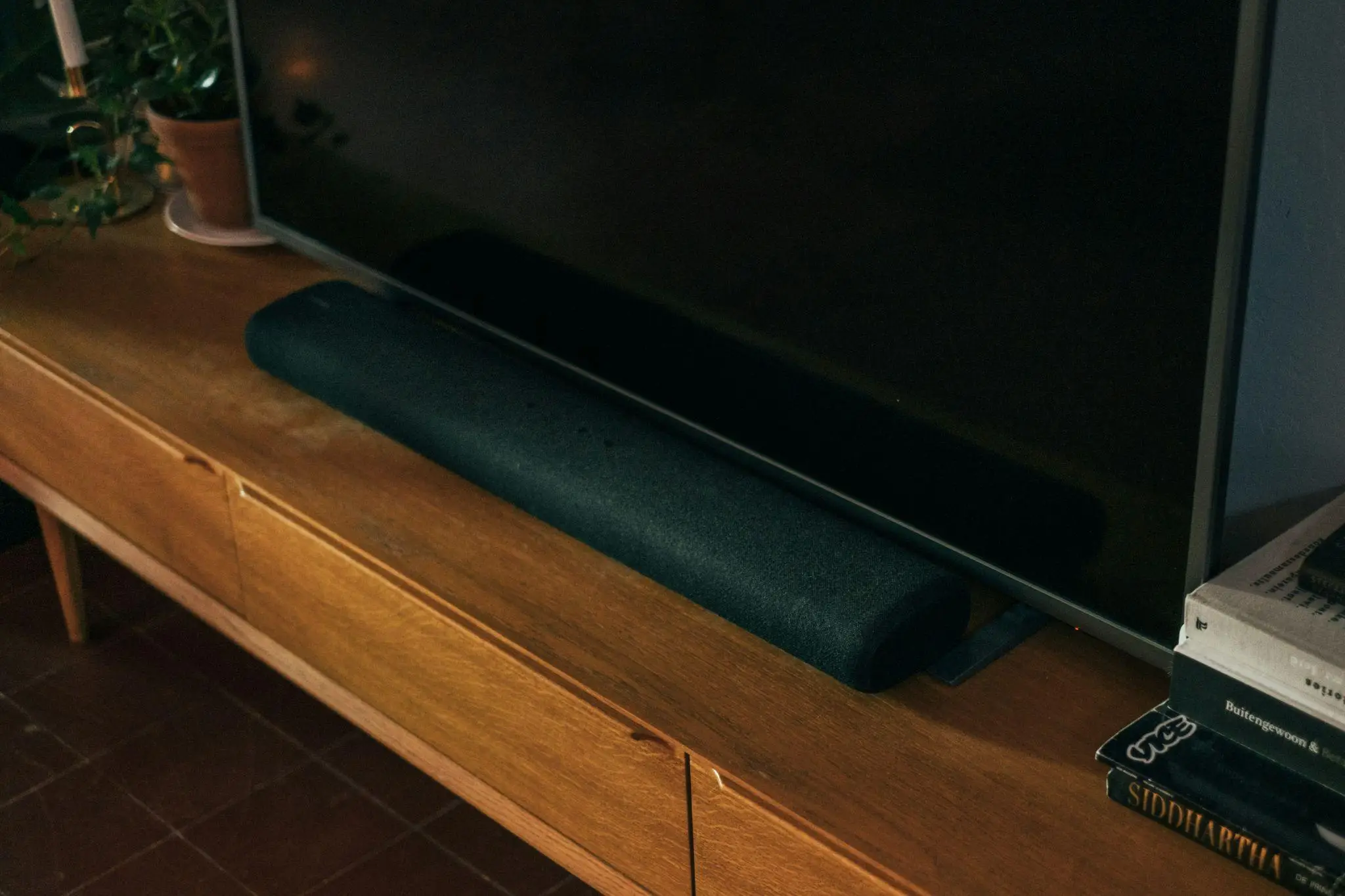 Soundbar placed on wooden media console under flat-screen TV in dimly lit room