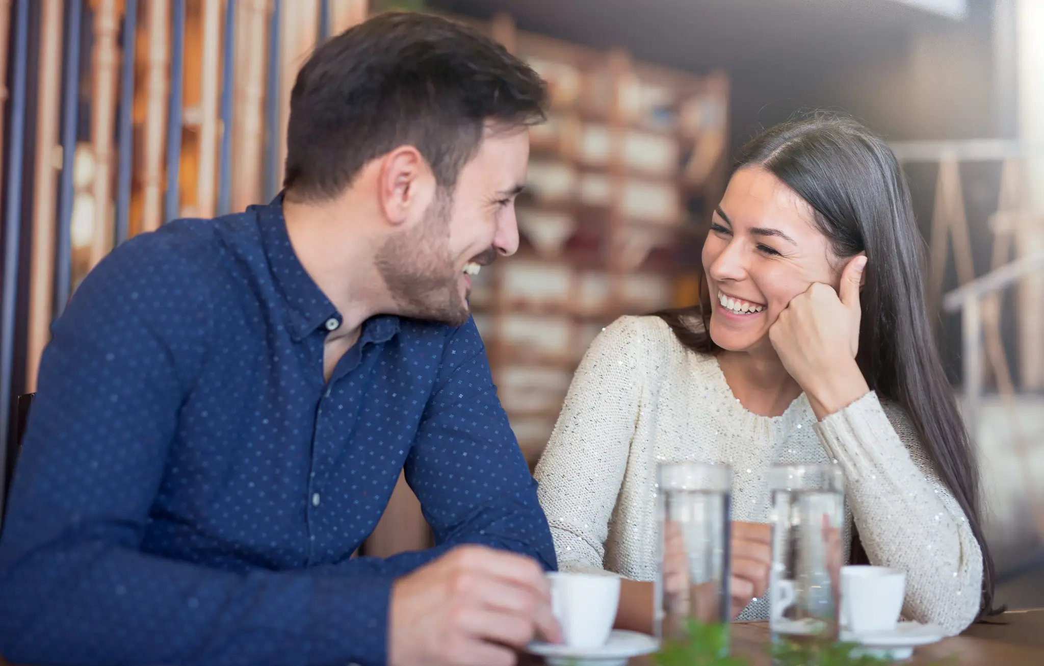A couple laughing together at a café table with coffee cups and water glasses