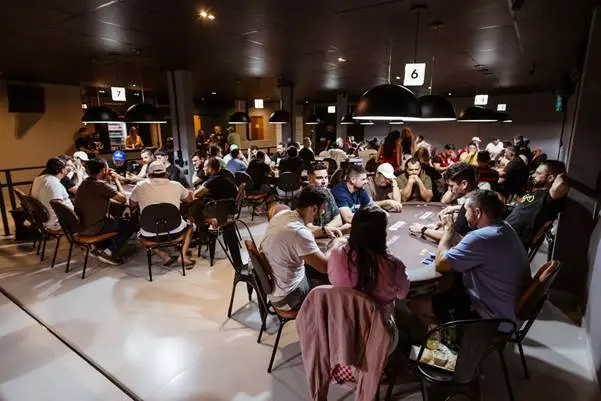 People playing poker at multiple tables in a dimly lit indoor gaming room