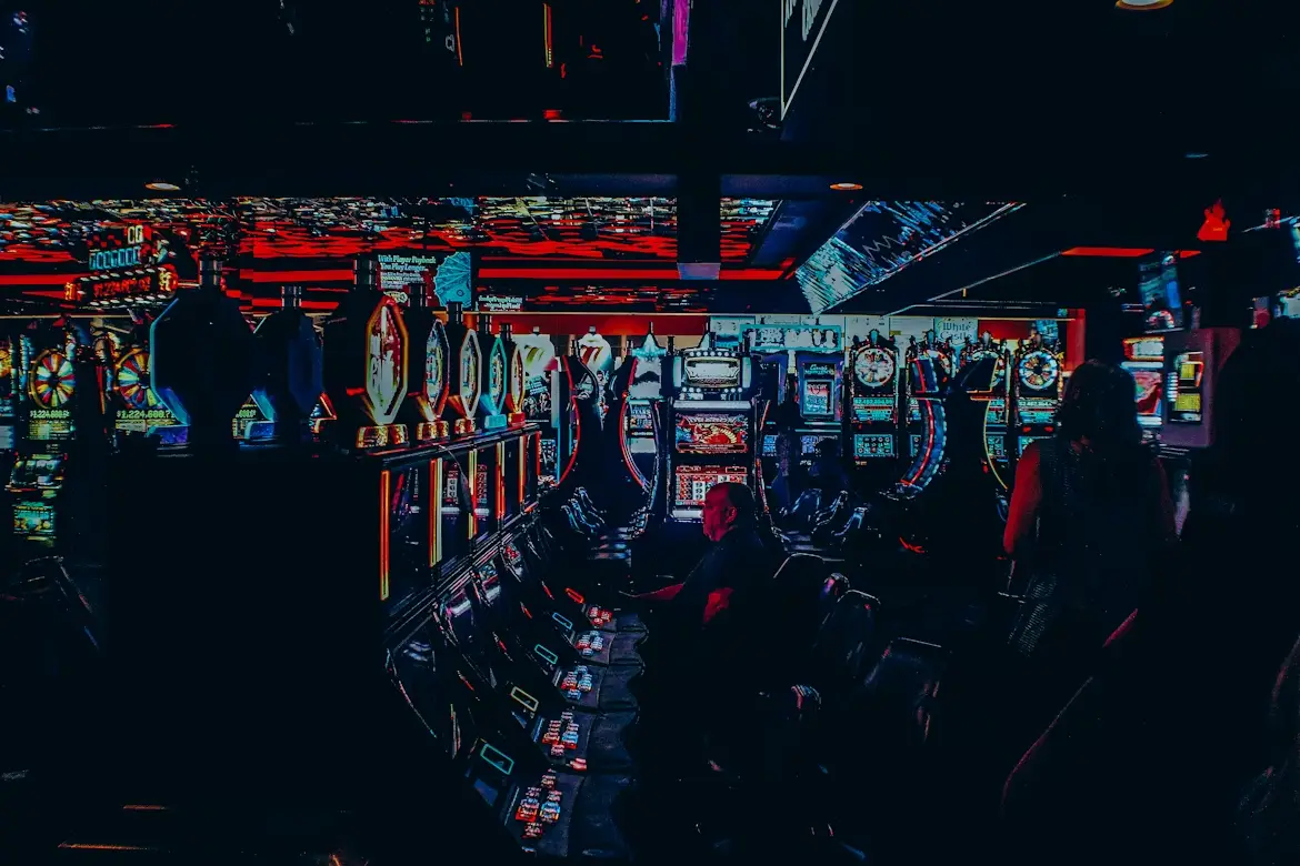 Slot machines illuminated in a dimly lit casino arcade with people playing