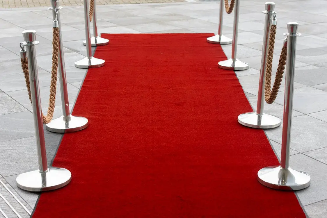 Red carpet walkway with silver stanchions and ropes on gray pavement