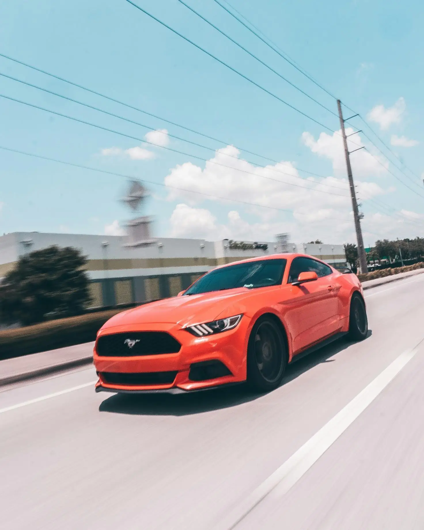 Red sports car driving on a sunny road with blue sky and clouds