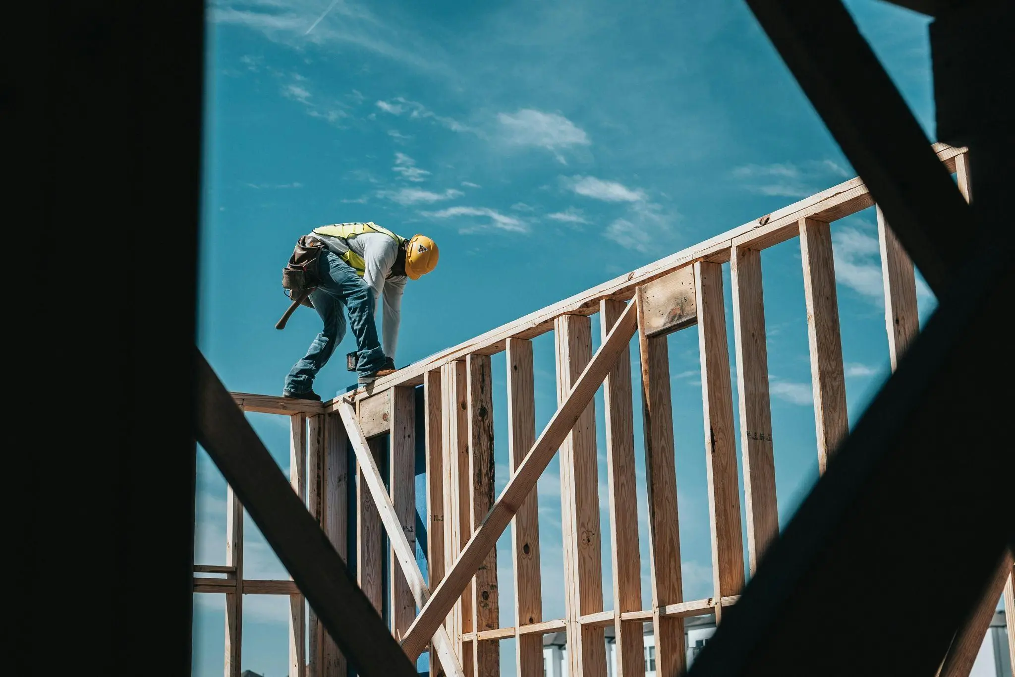 Construction worker in safety gear assembling wooden framework under blue sky