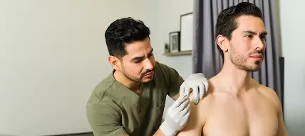 医療用手袋を着用した医療従事者が室内で男性の肩に注射しているところ