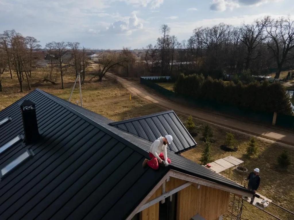 Construction workers installing black metal roof panels on wooden house in rural area