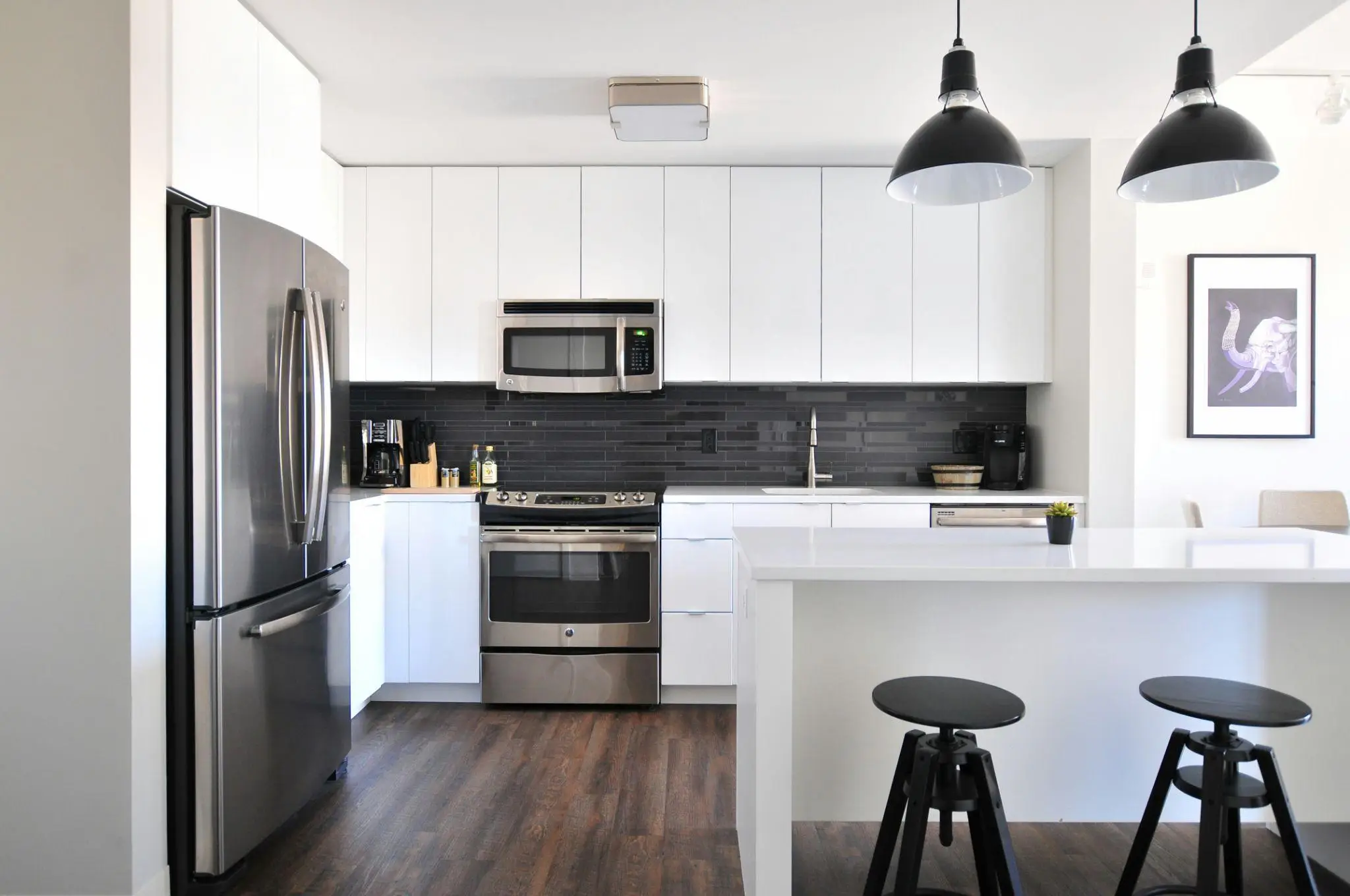 Modern kitchen with stainless steel appliances, white cabinets, and dark wood flooring