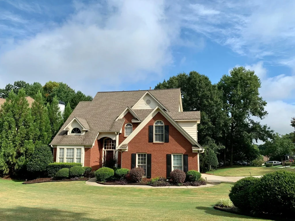 Brick house with steep gabled roof surrounded by manicured lawn and tall trees