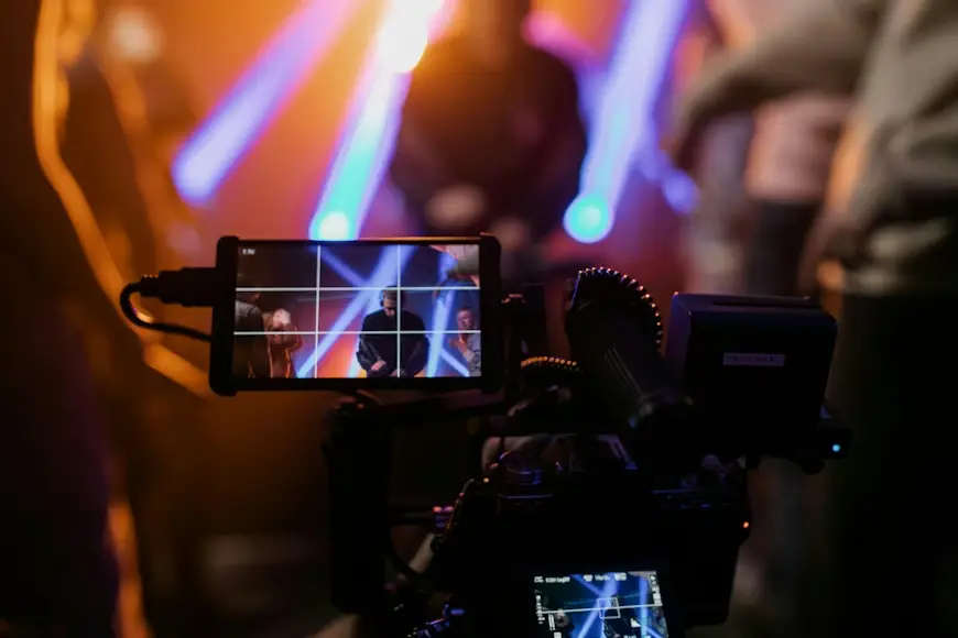 Camera filming concert with colorful stage lights and blurred musicians in background