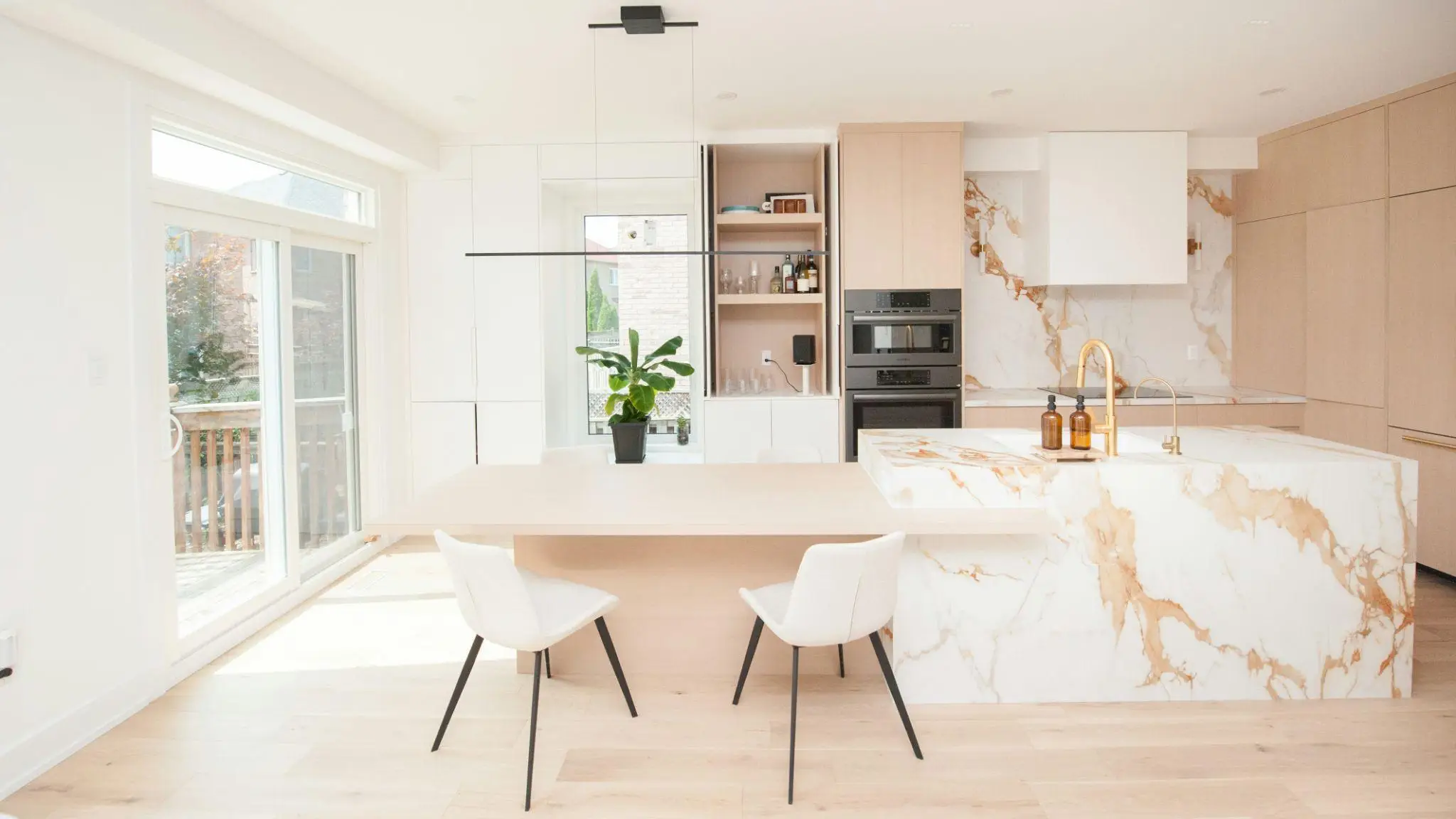 Modern kitchen with marble island, wooden cabinetry, potted plant, and natural light from large windows