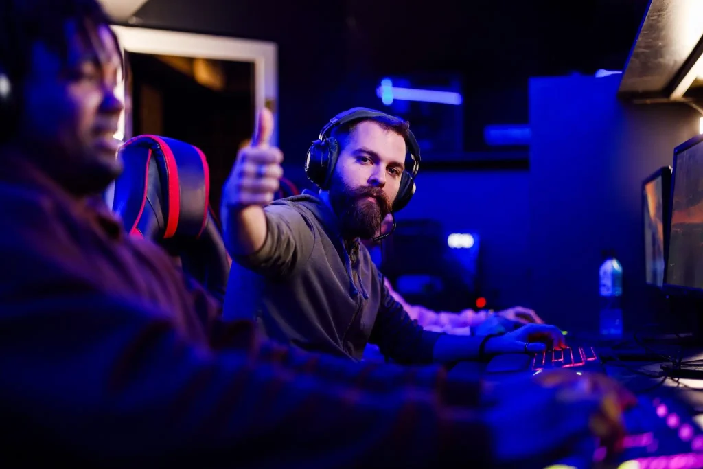 Gamer giving thumbs up while sitting at a computer in a dimly lit esports arena