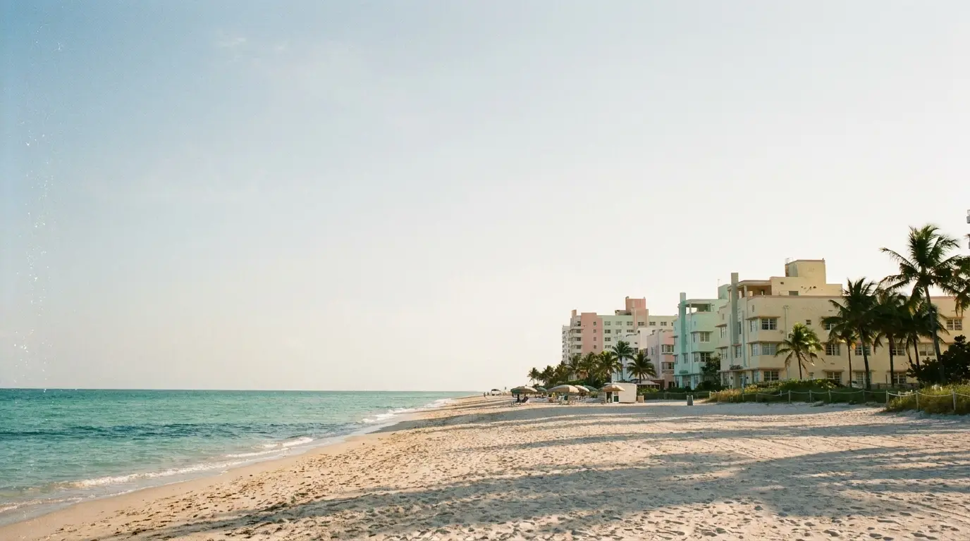 Pastel-colored beachfront buildings with palm trees and sandy beach under clear sky