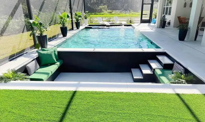 Modern backyard pool with green seating area and artificial grass under bright sunlight
