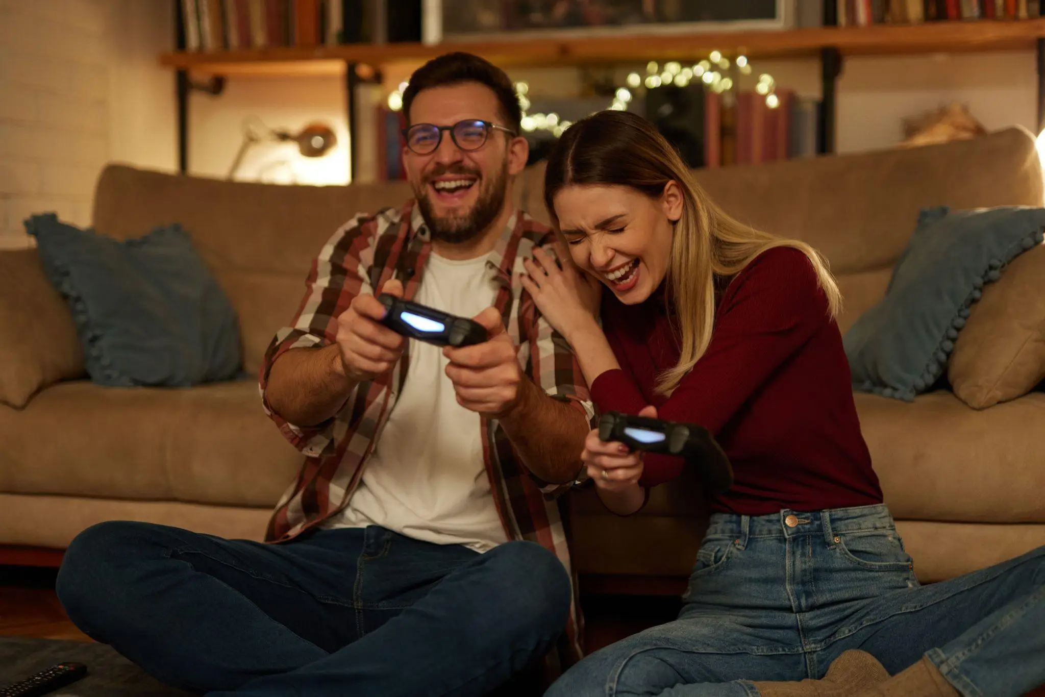 Couple laughing and playing video games on sofa in cozy living room