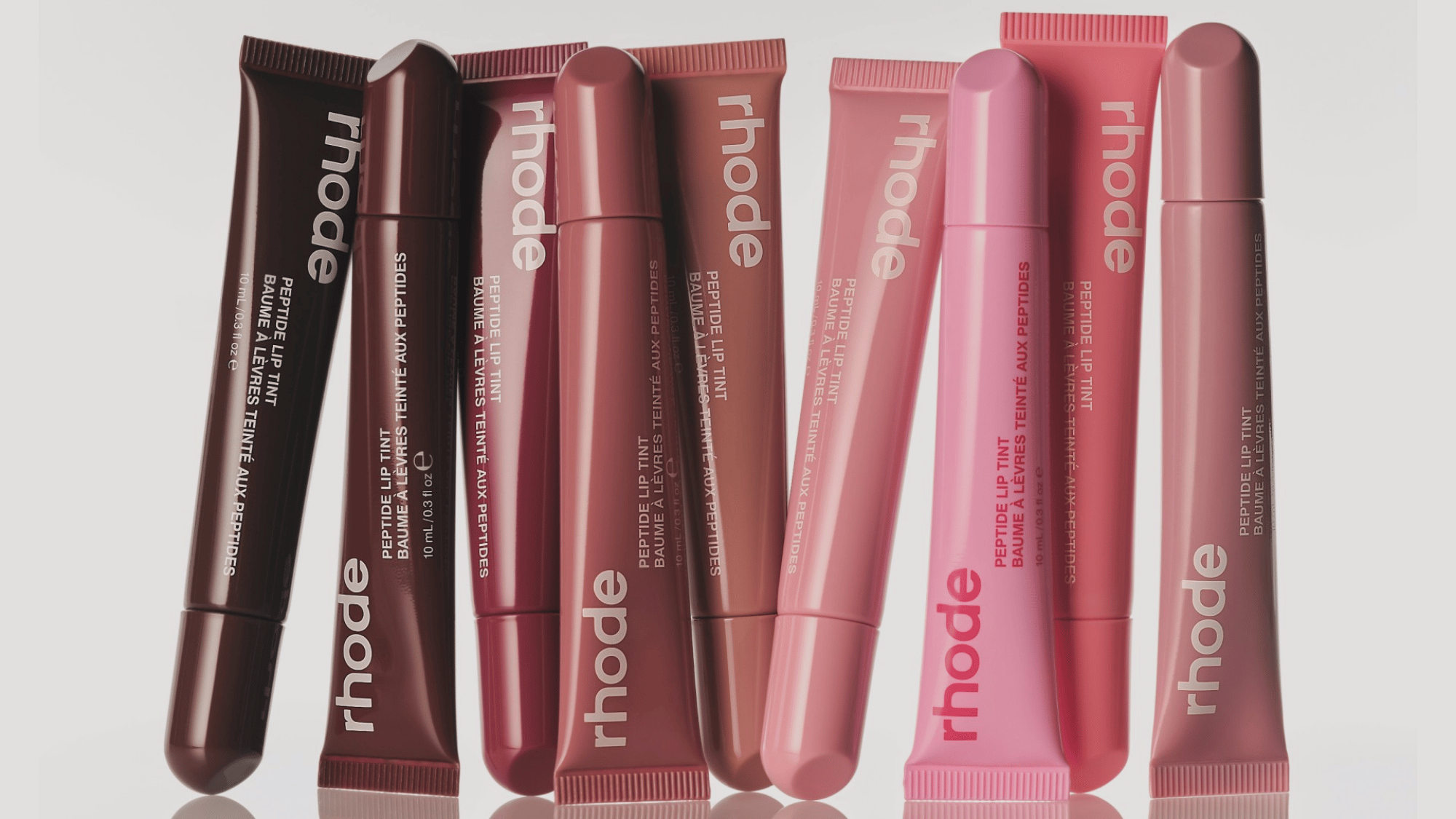 Collection of Rhode peptide lip tint products in multiple pink and brown shades displayed against a neutral background.