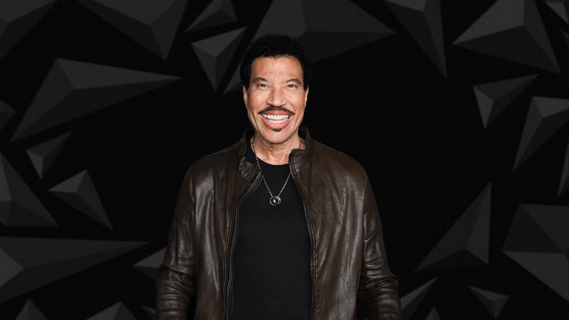 “Portrait of Lionel Richie against a solid black background, highlighting his face and signature smile with dramatic lighting for a sleek, elegant look.”