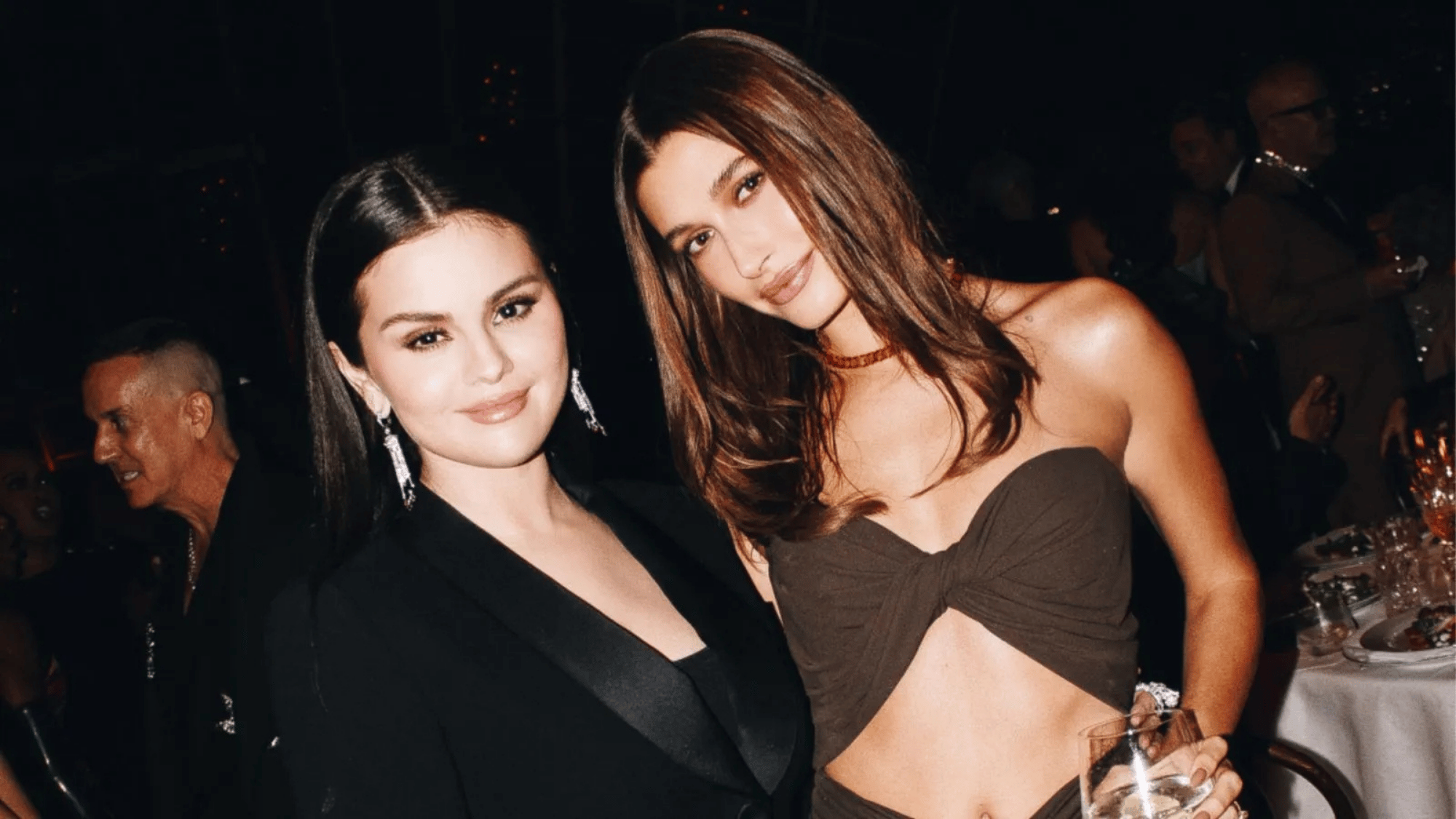 Selena Gomez and Hailey Bieber posing together at an evening event, both wearing glamorous outfits and smiling for the camera