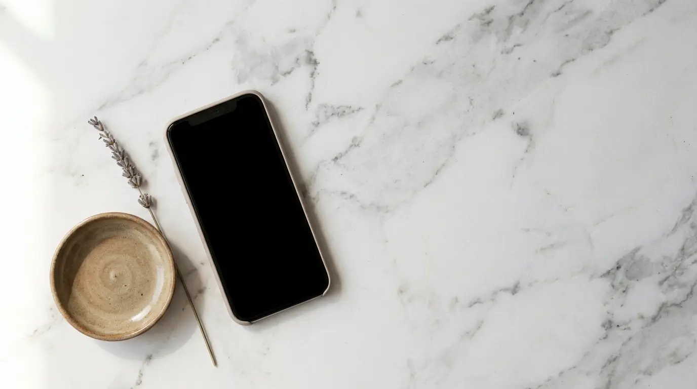 Smartphone with black screen on marble surface next to ceramic bowl and dried lavender
