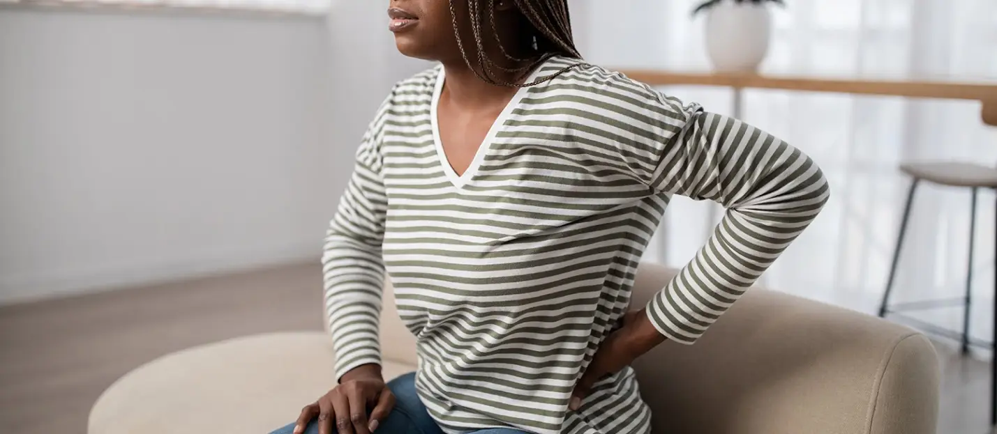 Person wearing striped shirt sitting on couch indoors holding lower back