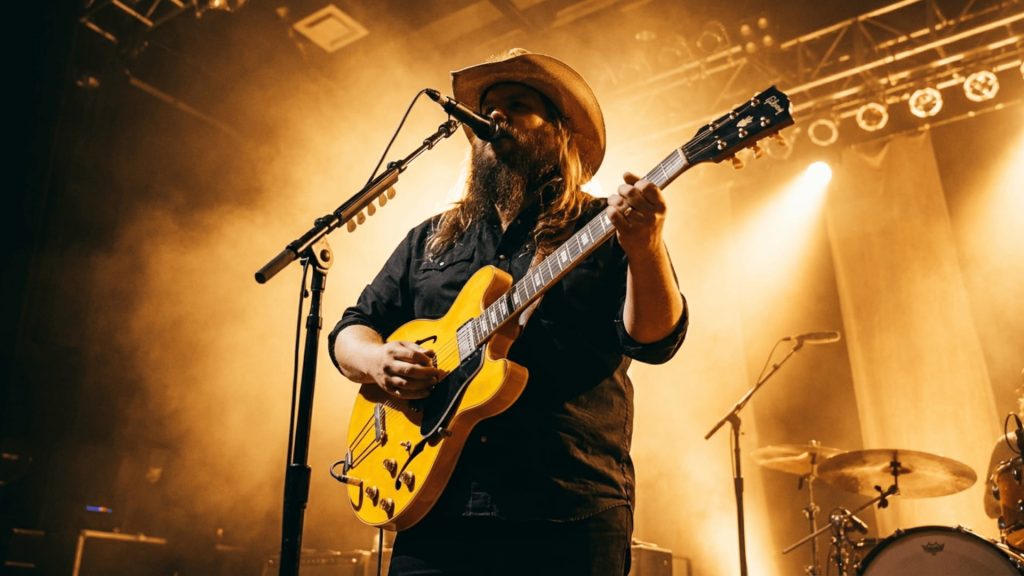country musician in black shirt and cowboy hat playing yellow hollow body guitar on stage with warm amber lighting