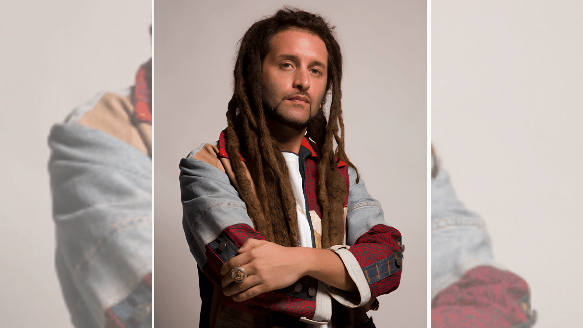 dreadlocked musician in patchwork denim jacket posing with folded arms in studio portrait.