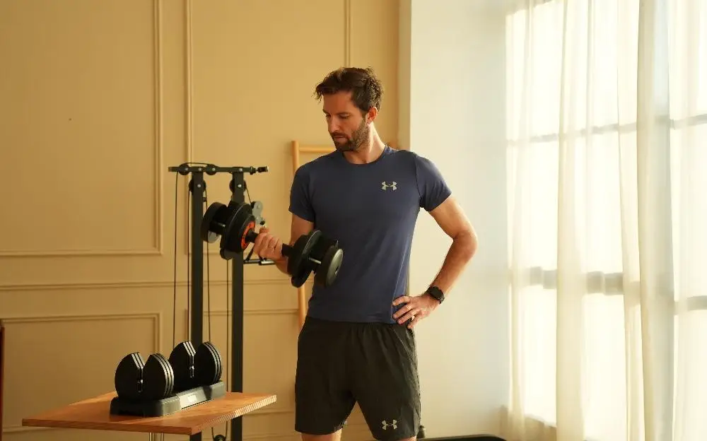 Man lifting dumbbell in home gym with beige walls and natural light