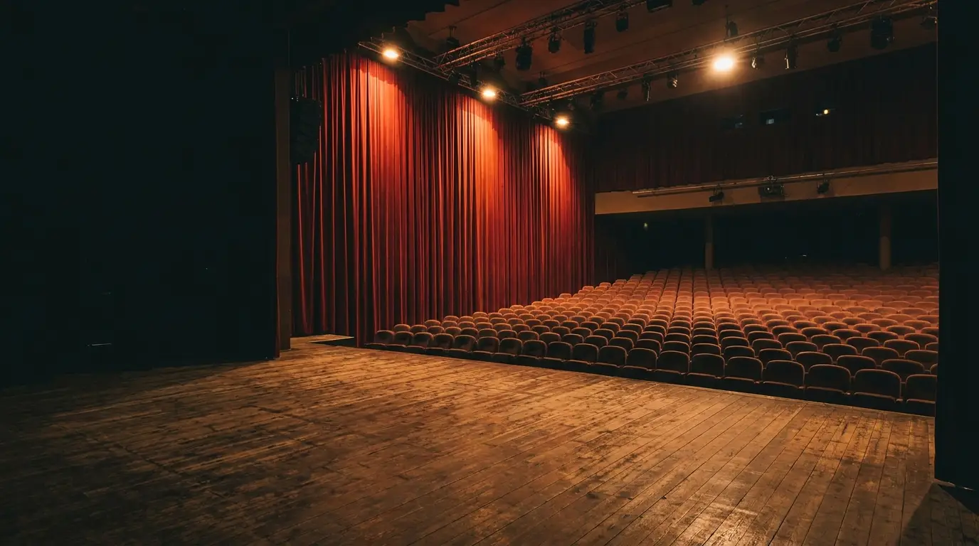 Dimly lit theater stage with red velvet curtains and empty audience seating