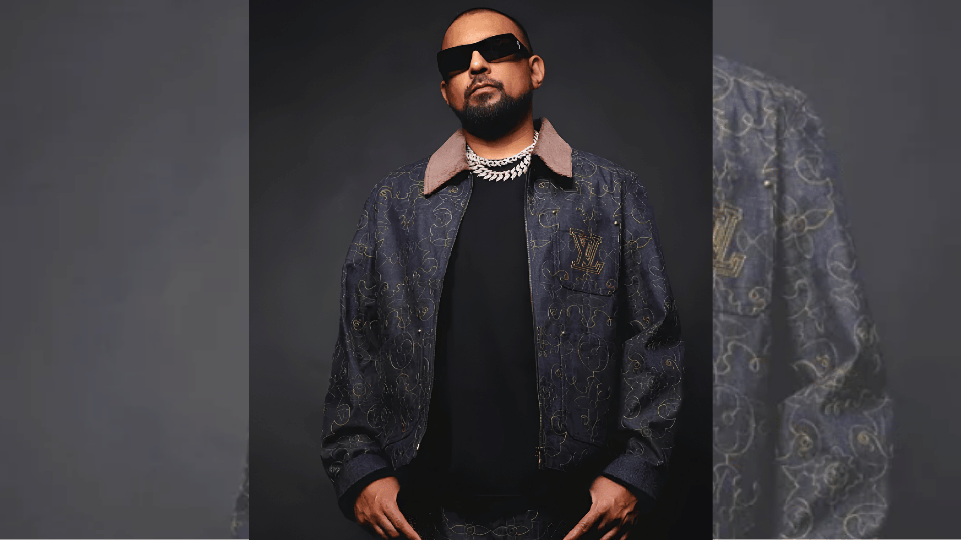 music artist in sunglasses and patterned designer jacket posing against dark studio backdrop.