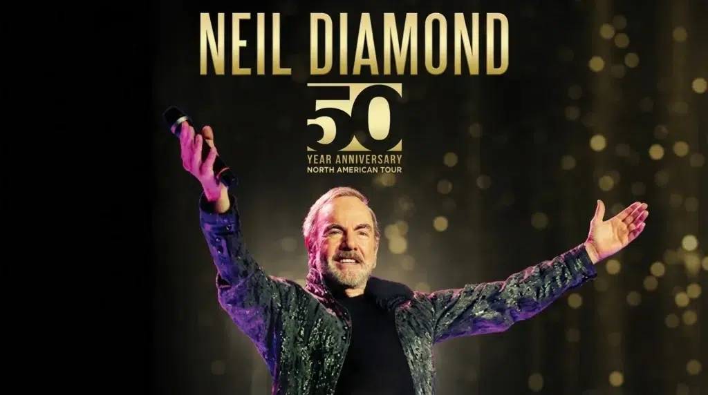 neil diamond performing on stage, on tour, holding a microphone with arms raised, smiling under a warm concert lights