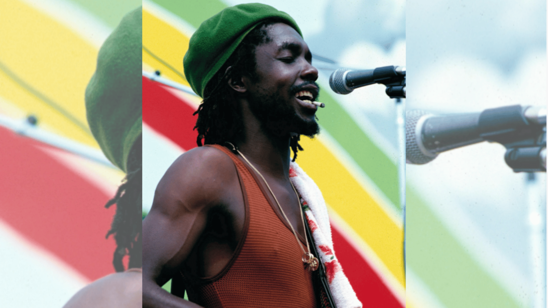 peter tosh singing into a microphone while playing guitar at an outdoor reggae music event