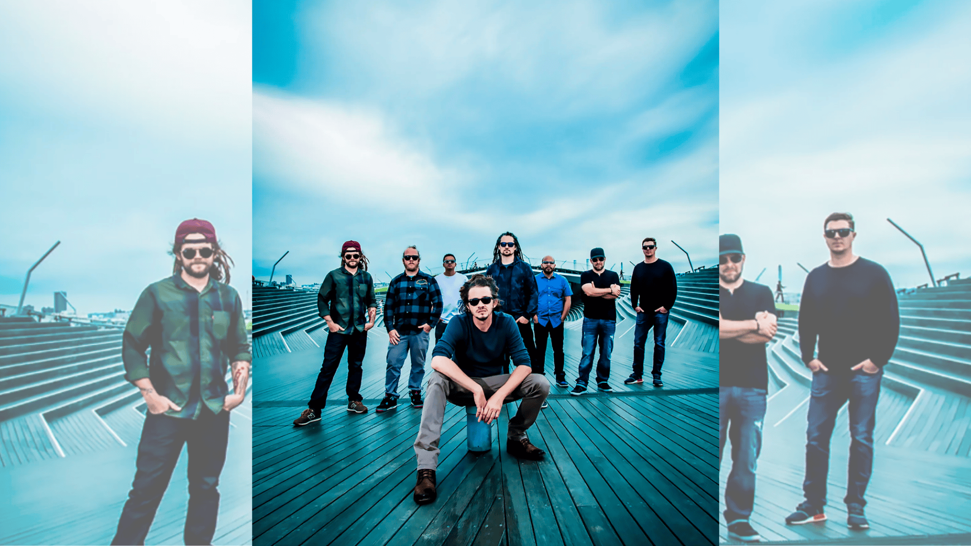 reggae fusion band posing on modern boardwalk under dramatic cloudy blue sky backdrop.