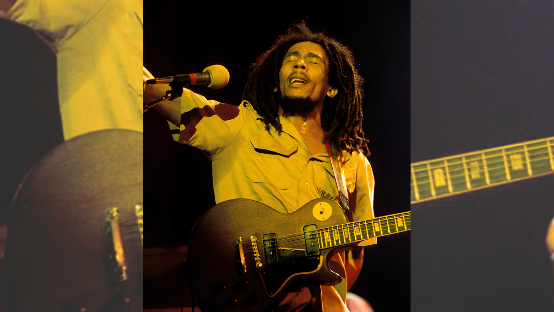 singer with dreadlocks raising arm while playing electric guitar under warm stage lights.