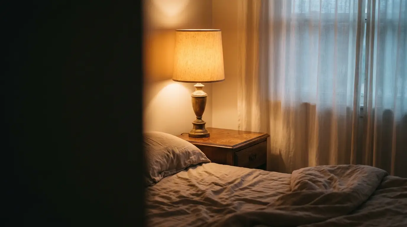 Cozy bedroom with lamp on wooden nightstand and soft lighting next to window with sheer curtains