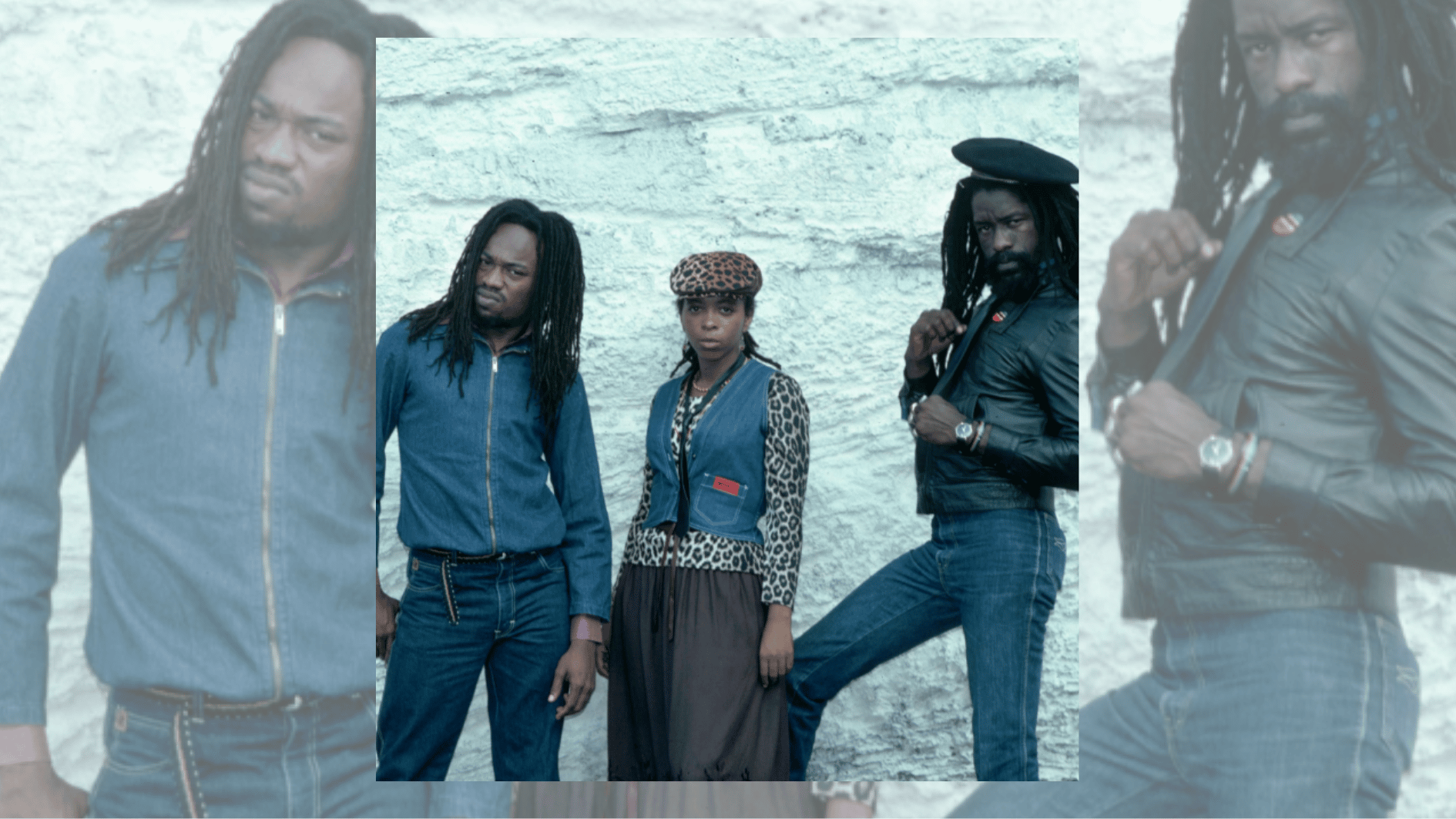 three people with dreadlocks and patterned clothing posing against rough white stone wall.