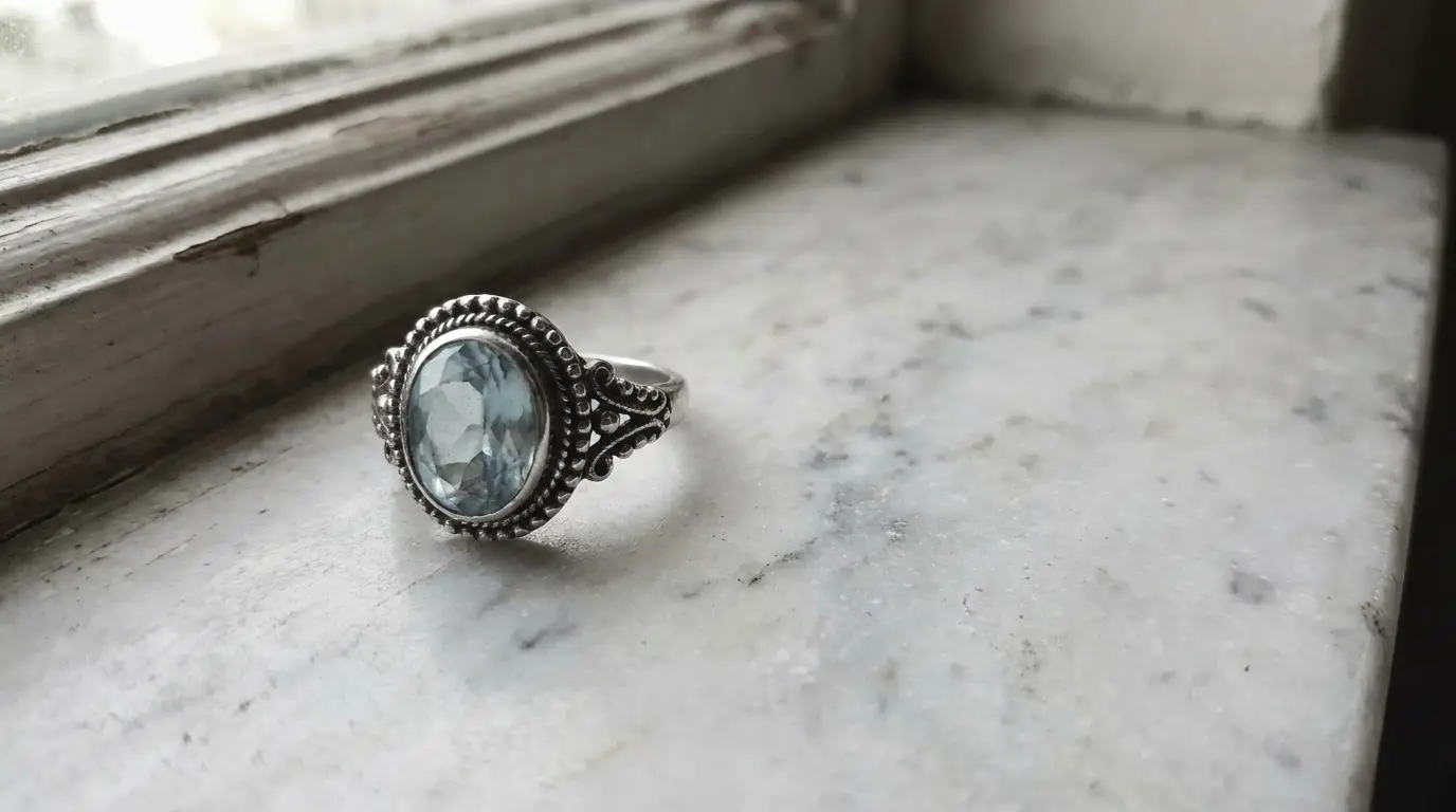 Silver ring with blue gemstone on marble windowsill in soft natural light