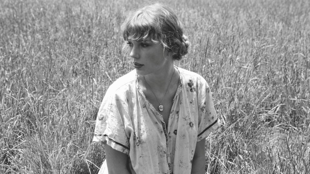 woman in floral dress sitting in tall grass field, black and white photography, soft natural light, candid mood