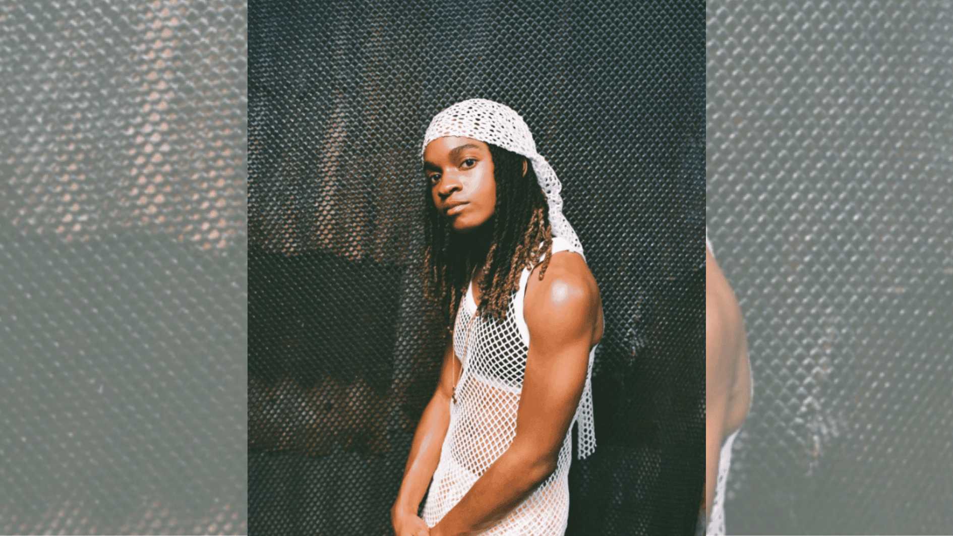 young performer in white mesh outfit and headscarf posing against textured dark backdrop.