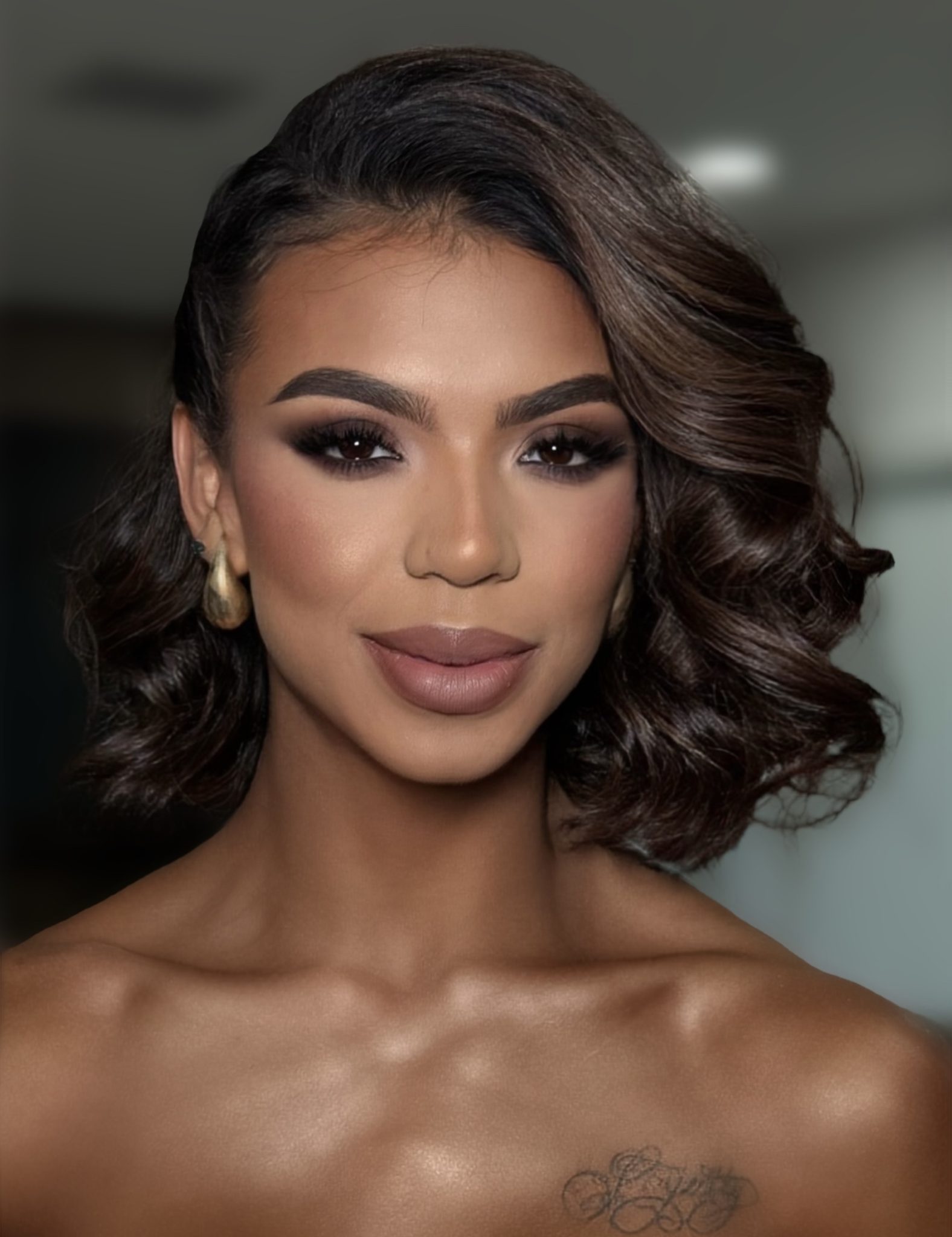 Young woman with styled wavy hair and makeup smiling indoors