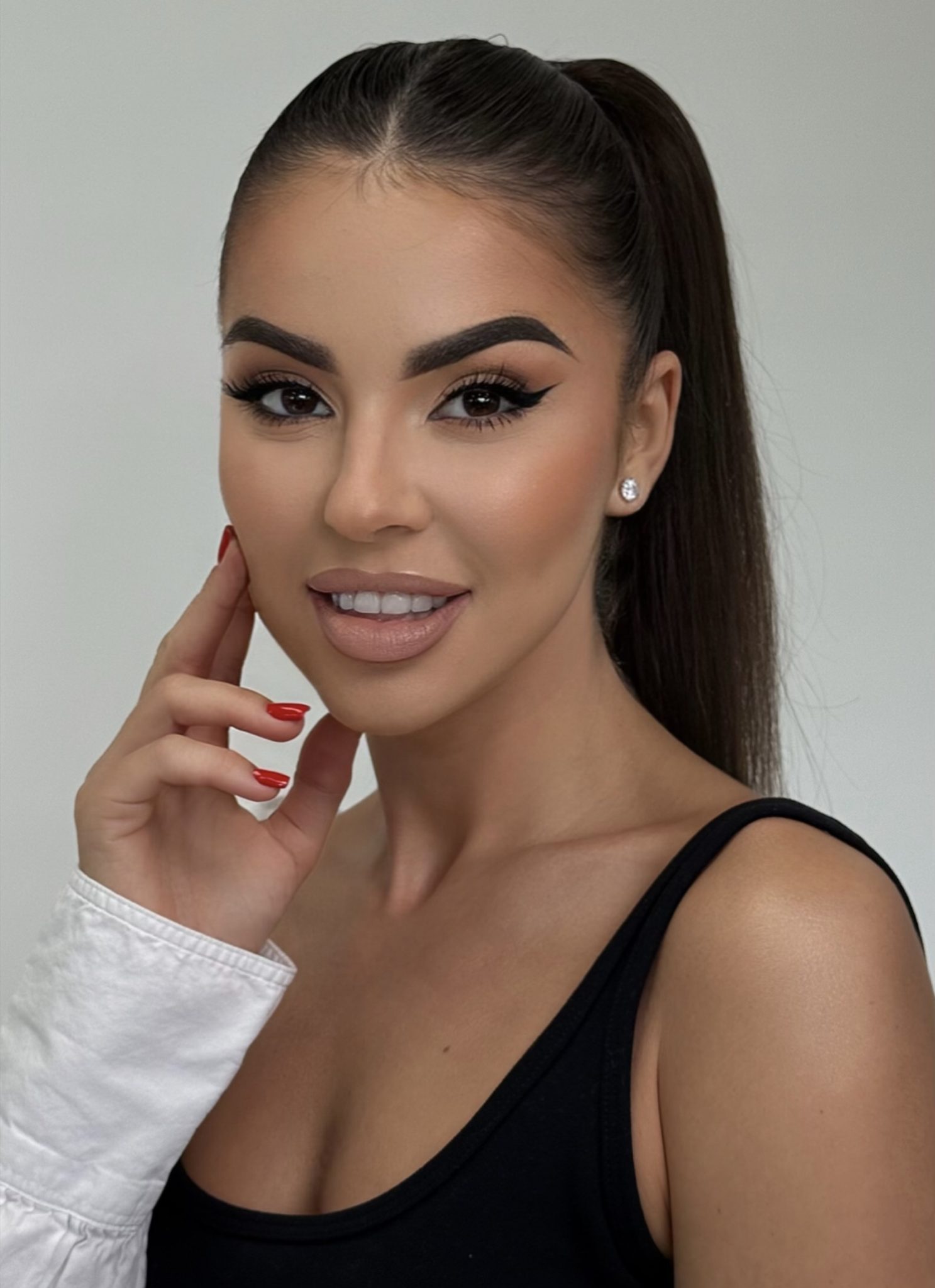 Woman with sleek ponytail and red nails smiling against plain background