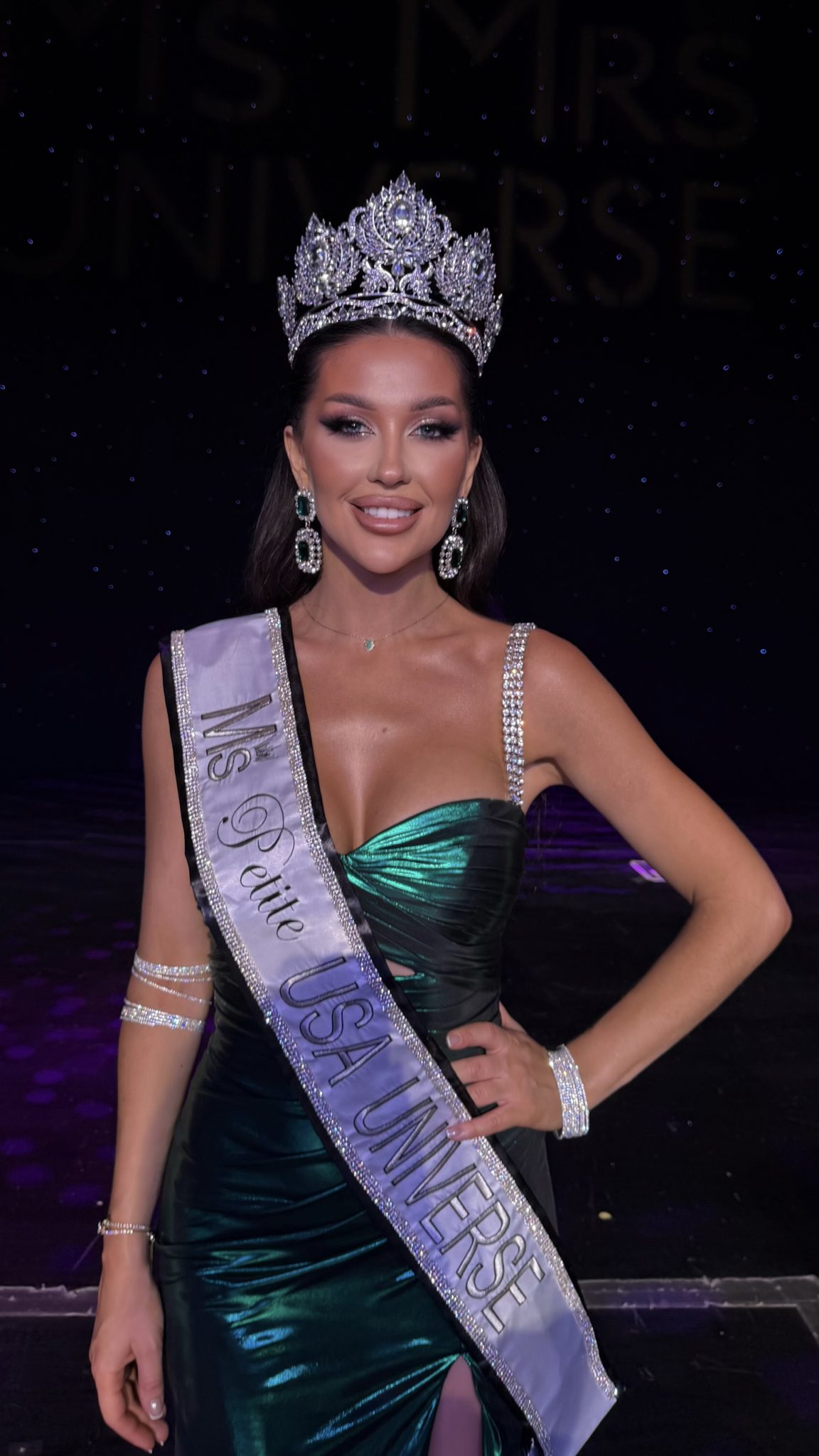 Beauty pageant winner in emerald gown and jeweled crown on stage with spotlight background