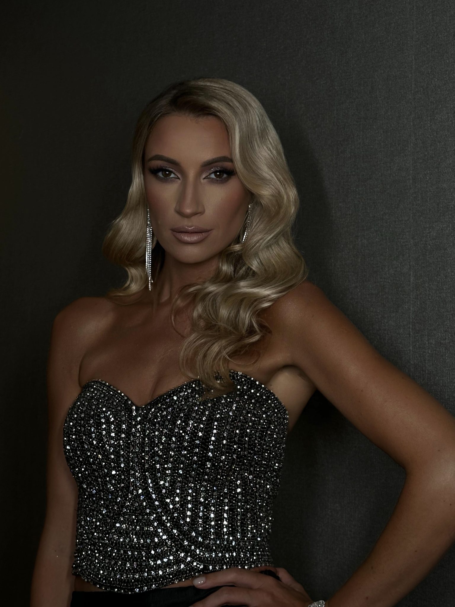 Woman in a sparkling black gown with wavy blonde hair against dark background
