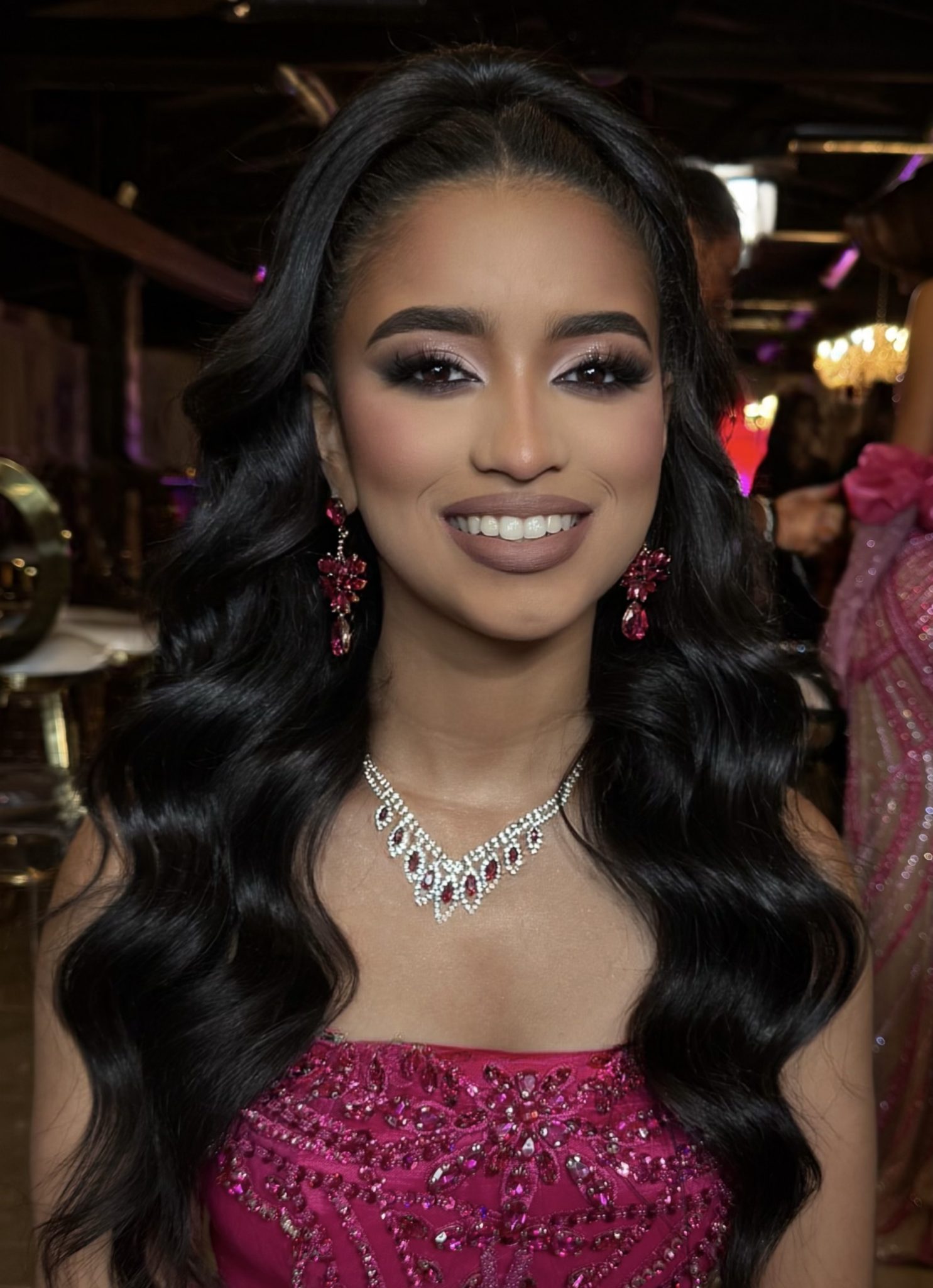 Woman with long black hair wearing elegant red jewelry in a dimly lit indoor setting